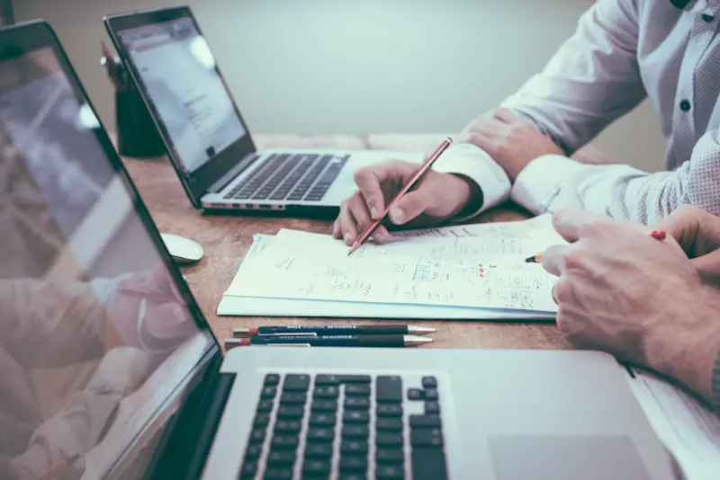 Manos con lápiz analizando documentos y notebooks sobre un escritorio de trabajo